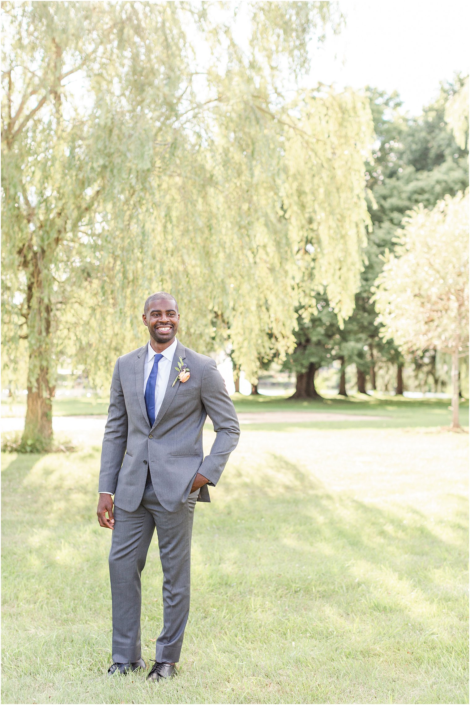 Groom standing by willow tree during wedding editorial 