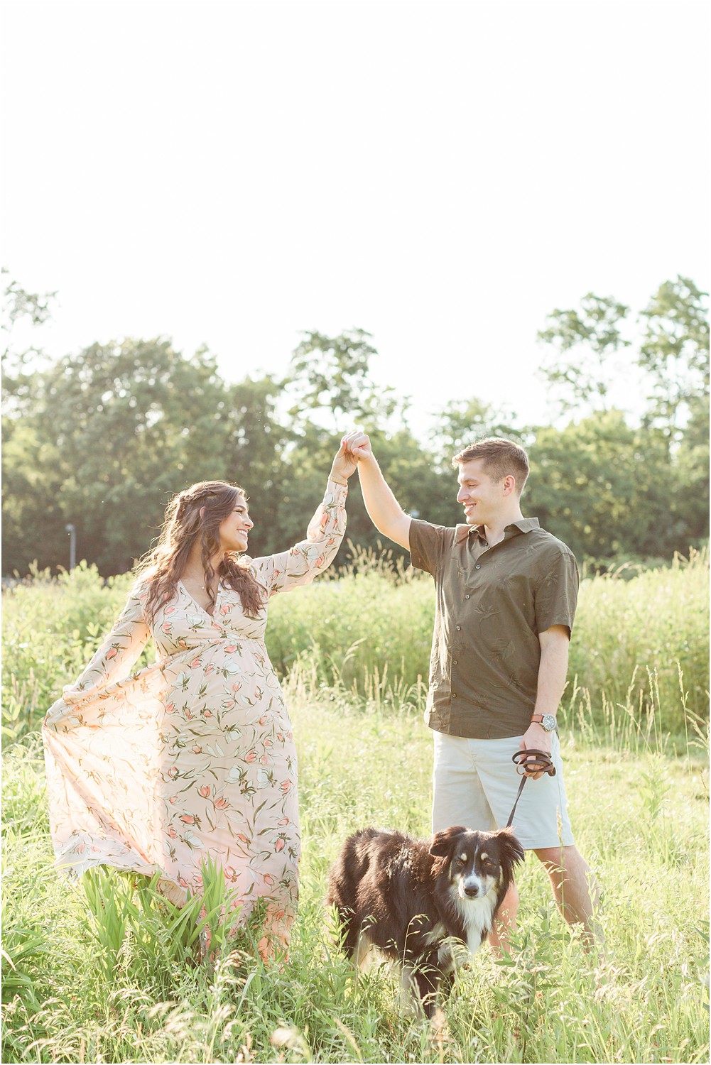 husband and wife twirl in grass with their dog during outdoor maternity session