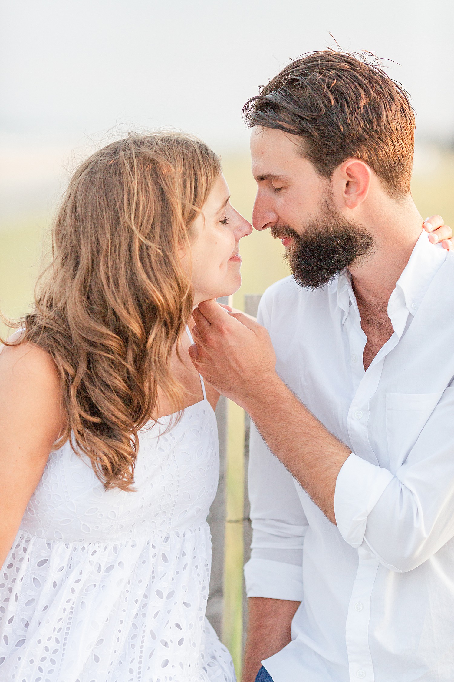 couple styled in neutral clothing lean in for a kiss during engagement photos