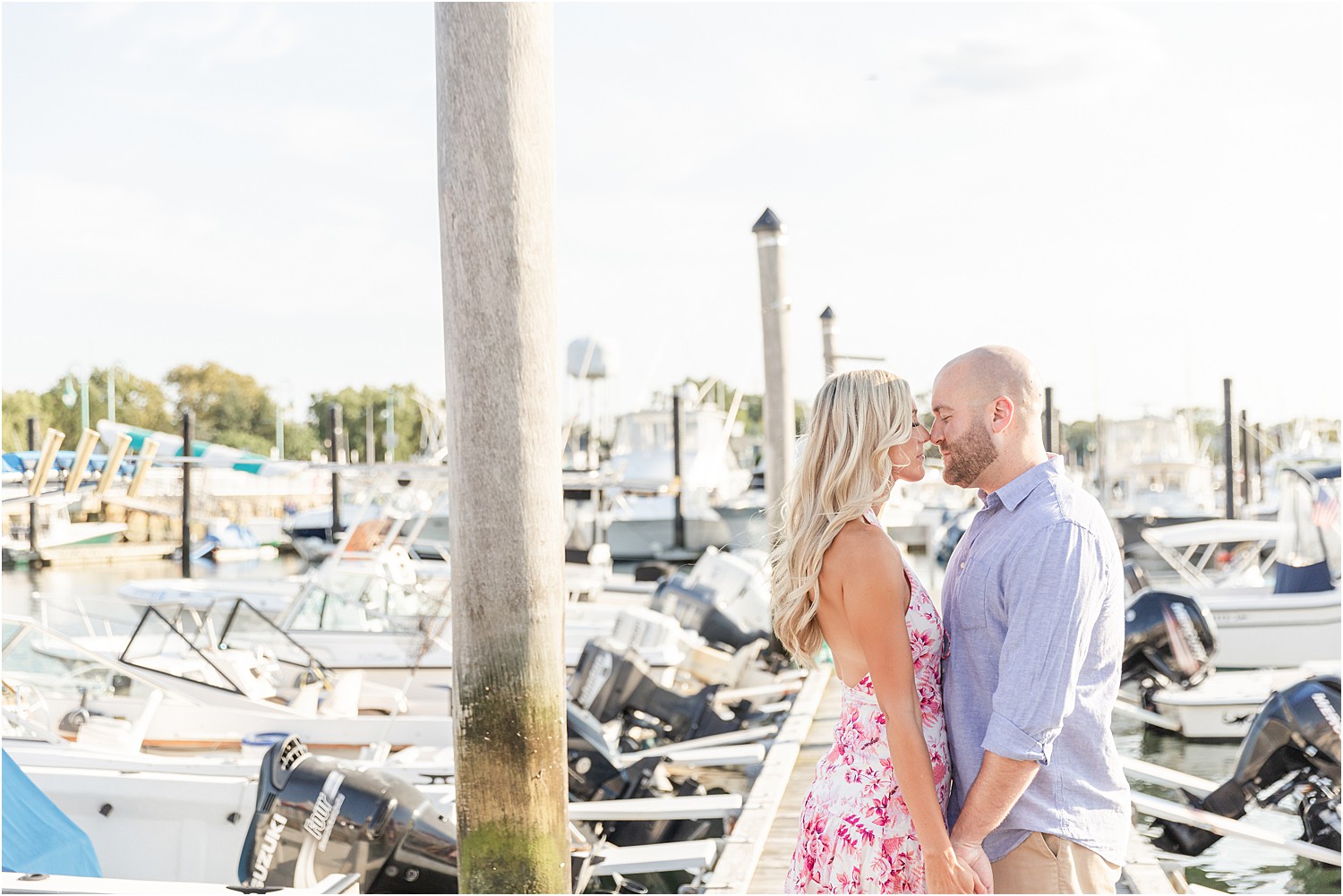 Engaged couple kiss at marina with boats in background
