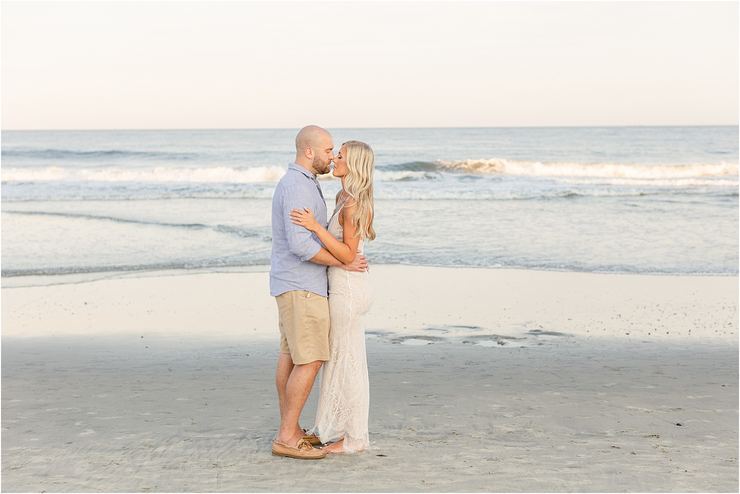 woman in white bohemian dress kisses her fiance at the beach