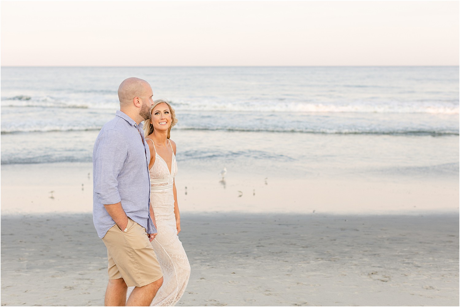 woman looks up at fiance as they walk along NJ beach