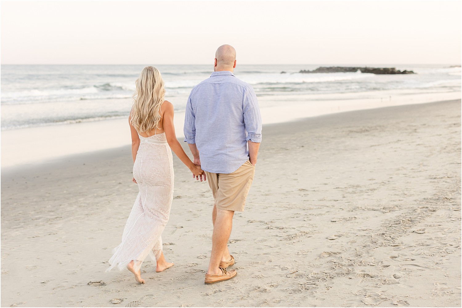 couple walk down the coastline holding hands at Belmar beach in NJ