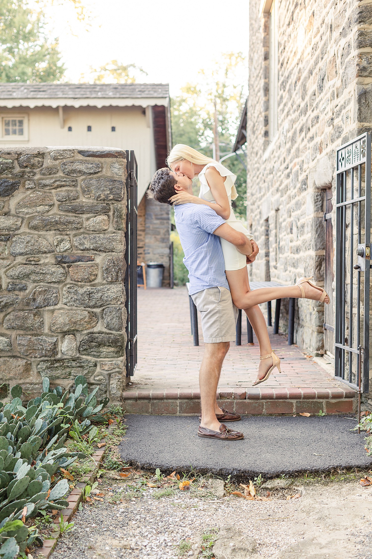guy picks up fiance near iron gate and stone wall at Bartram’s Garden