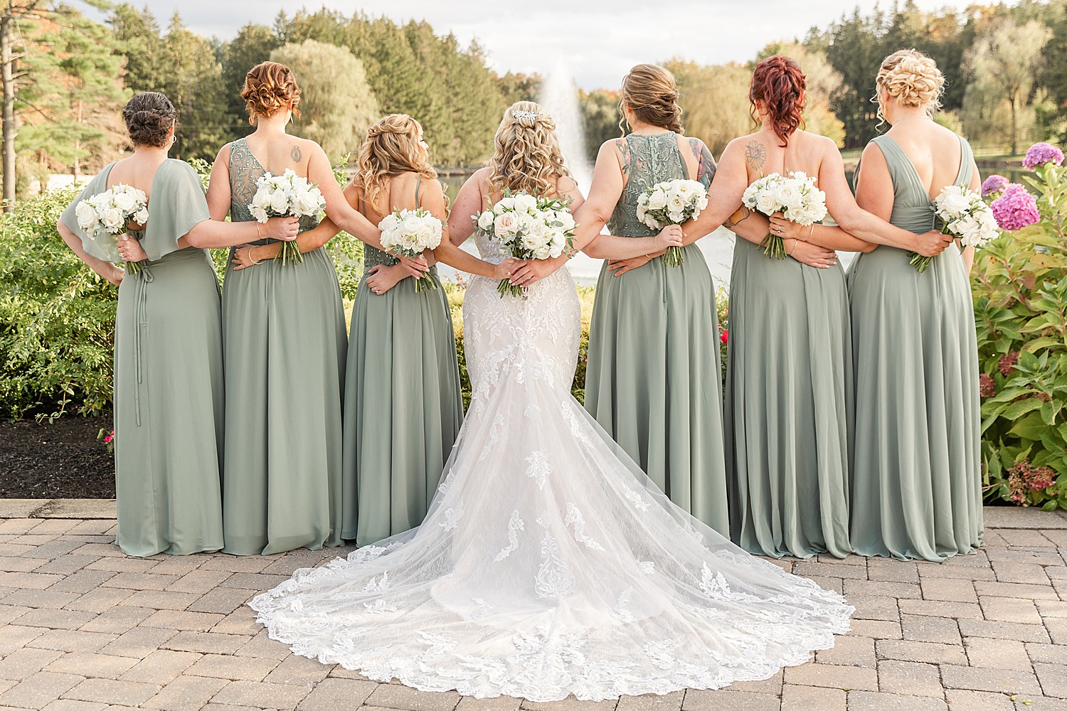 bride and bridesmaids link arms and show off back of dresses  