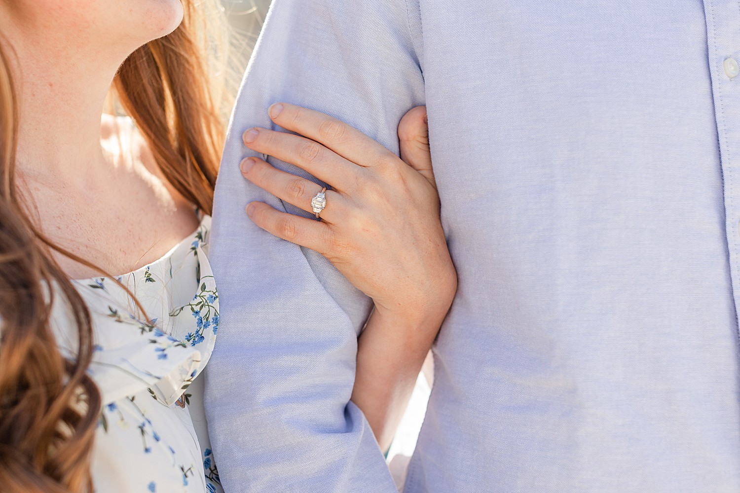 woman wraps hand around man's arm showing off engagement ring