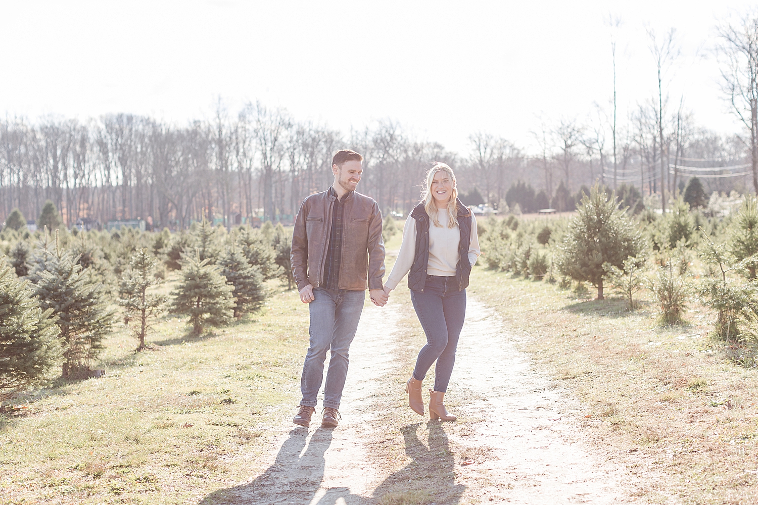 engaged couple walk together holding hands at Christmas tree farm