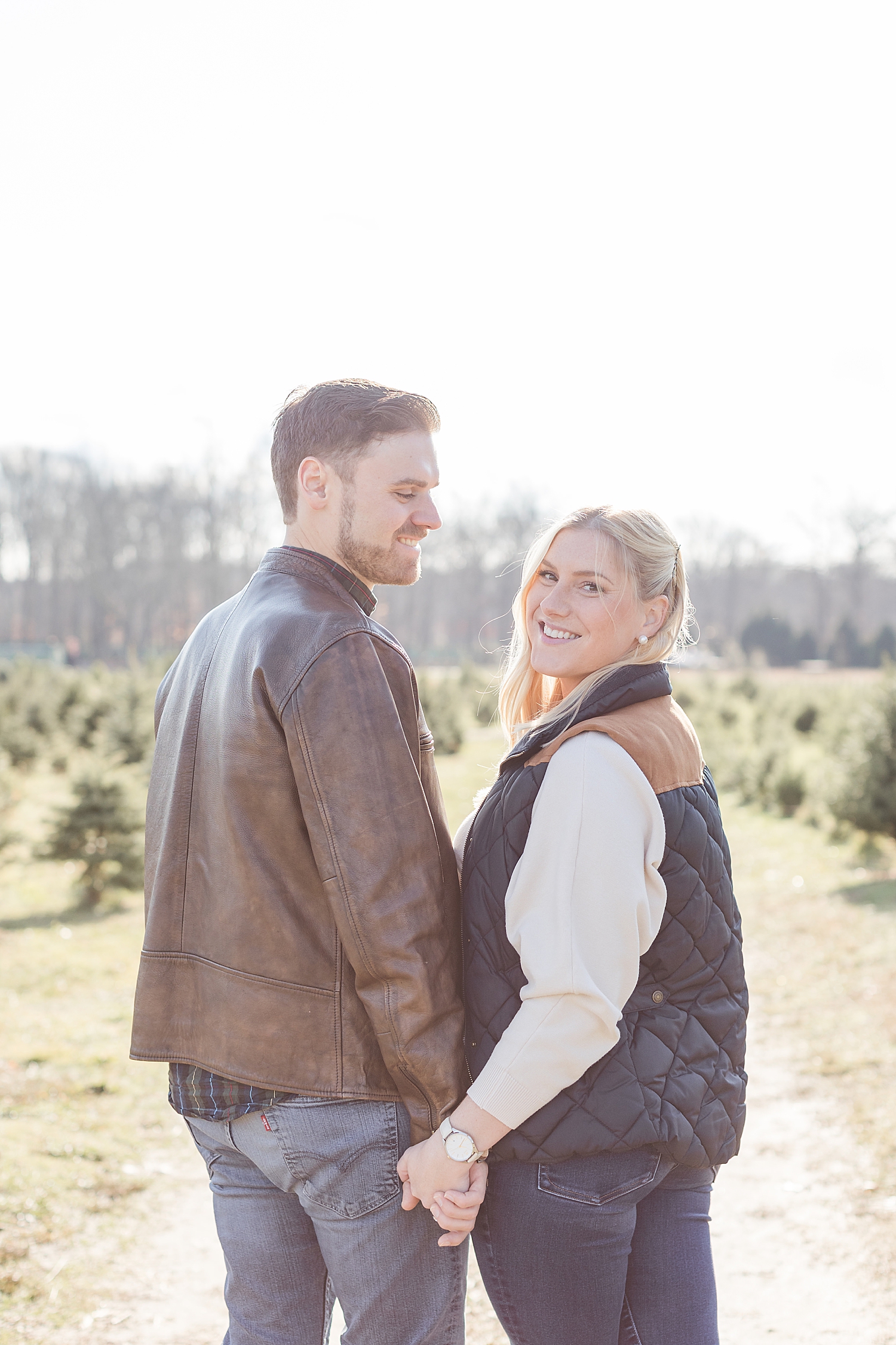 couple hold hands as they explore a Christmas tree farm