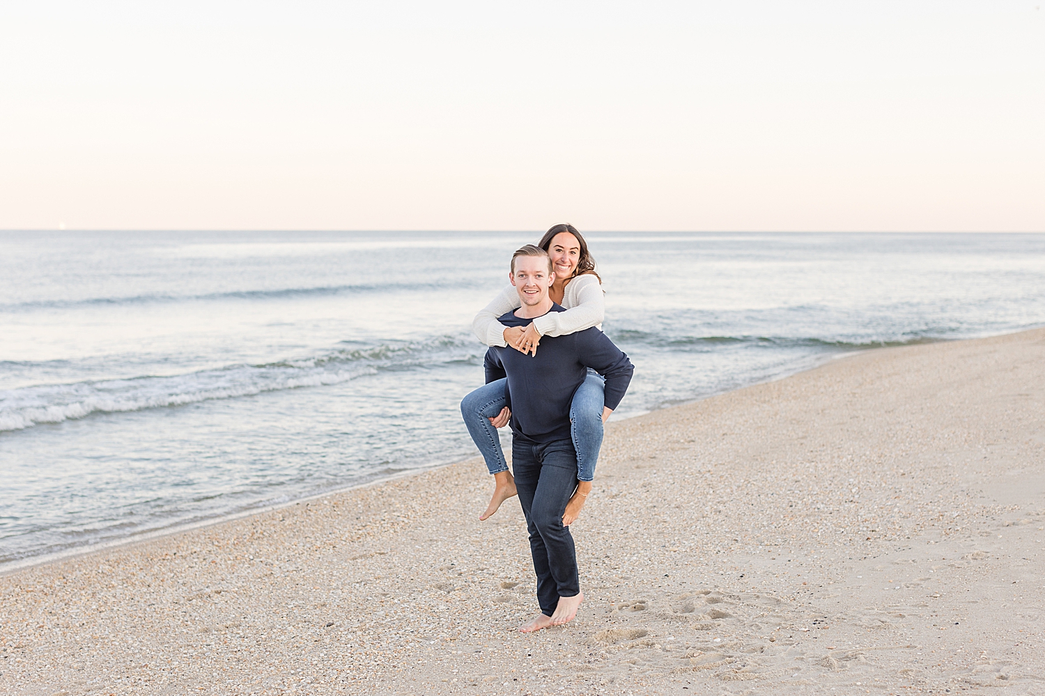 man carries his fiance on his back at the beach