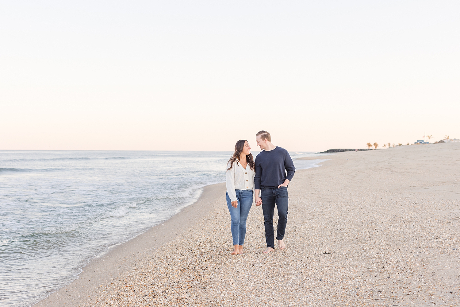 engaged couple walk together along the ocean shoreline