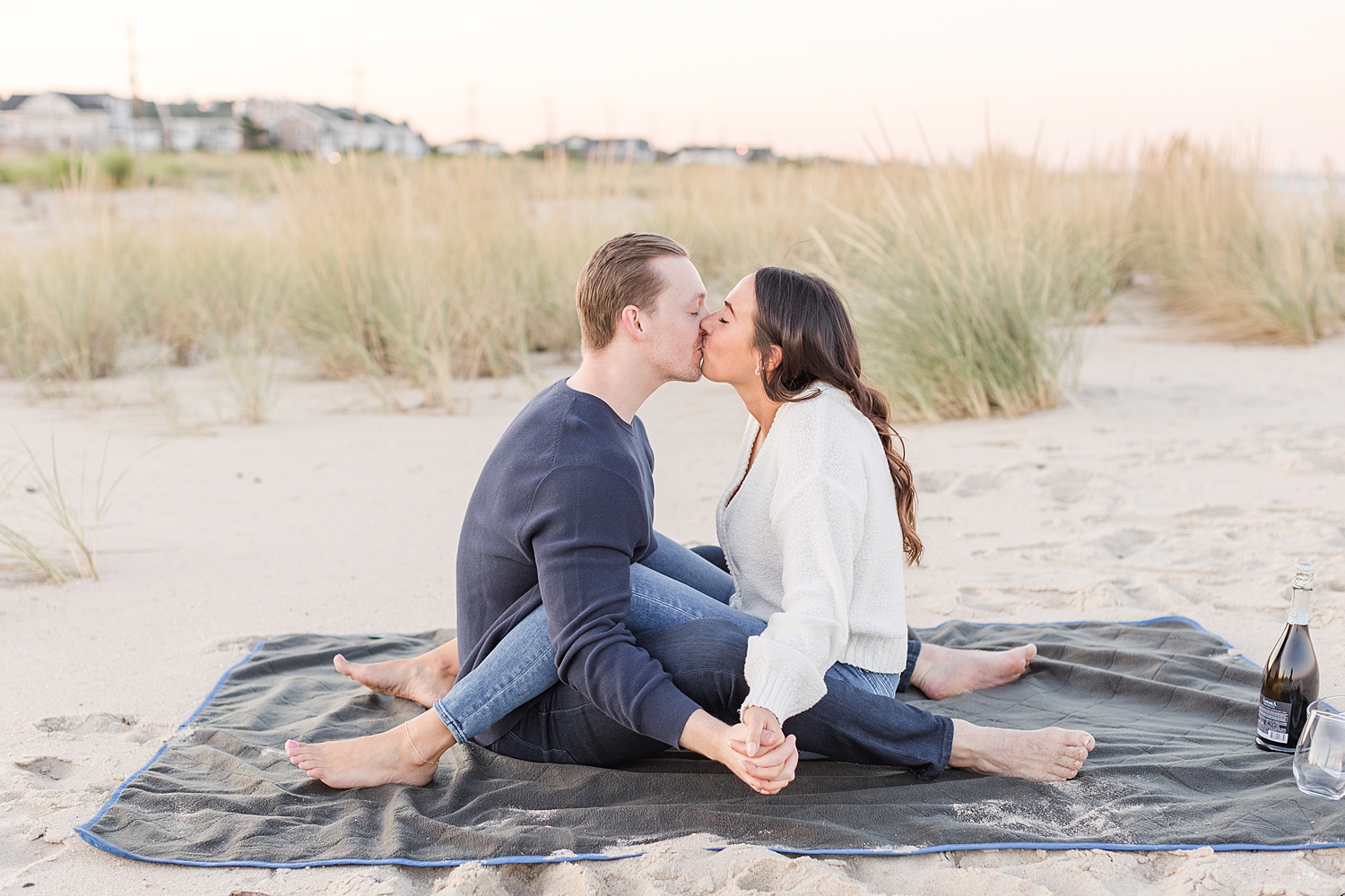 engaged couple sit on blanket at the beach