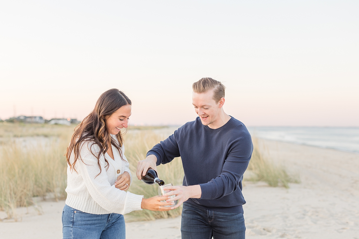 man pours champagne during New Jersey engagement session on the beach