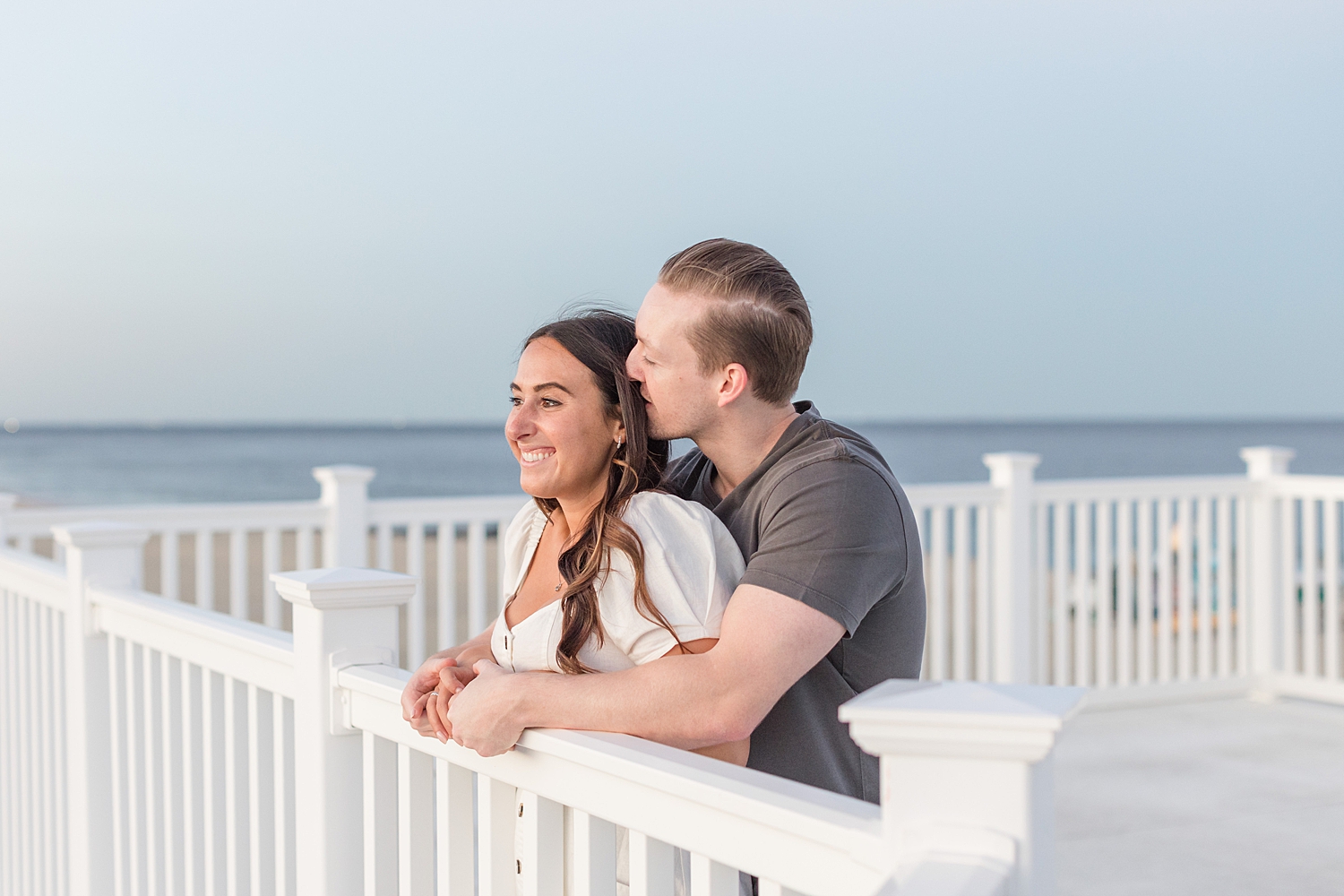 couple leans over balcony as man kisses his fiance's head