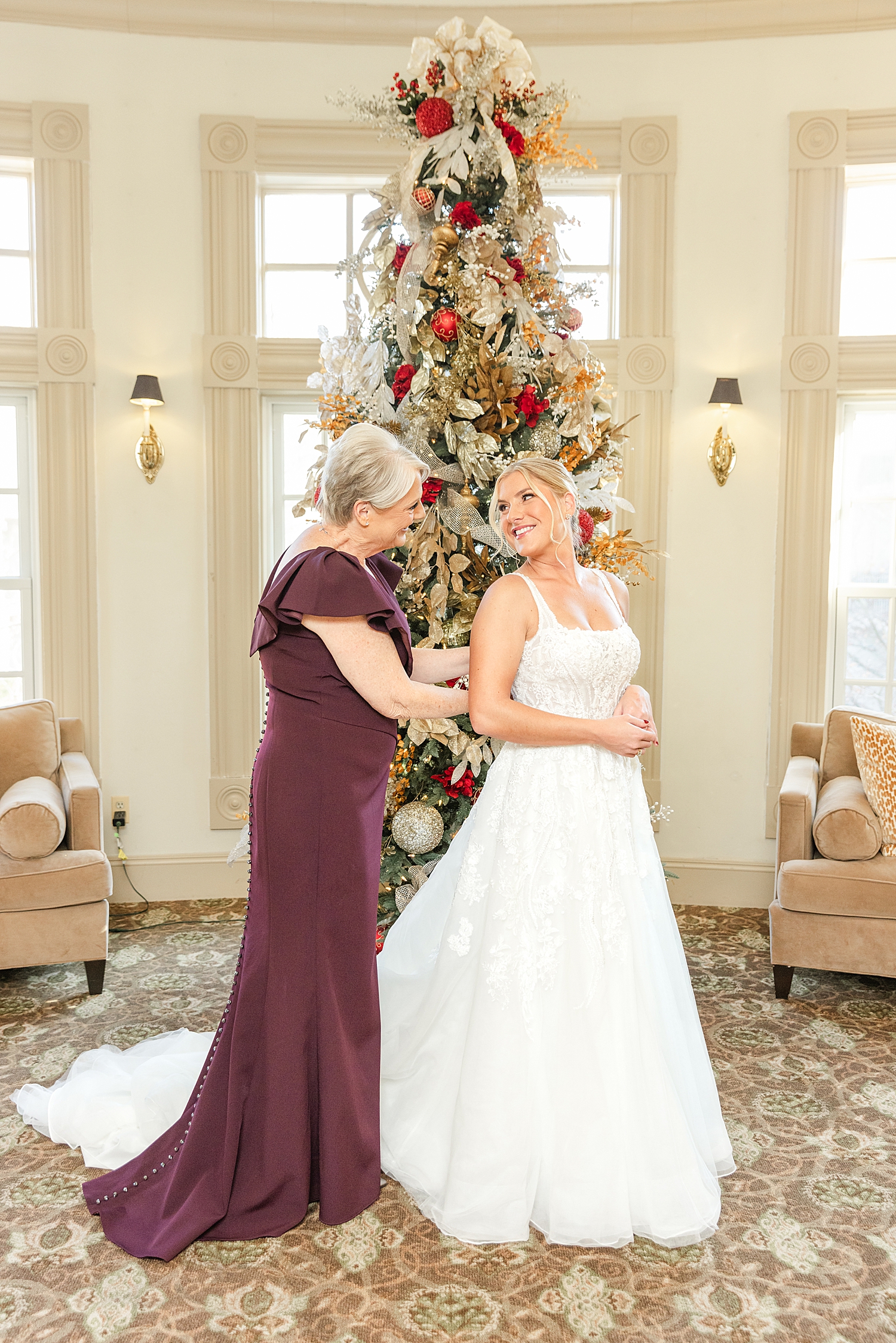 mom helps daughter into wedding dress in front of Christmas tree